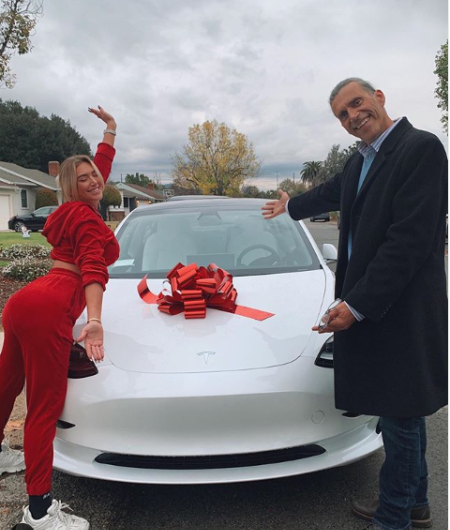 stassie and her dad standing infront of the new tesla car she bought her 